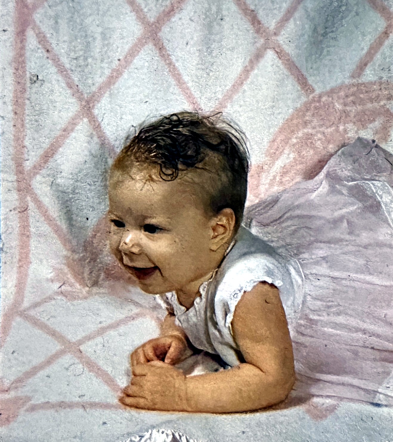 A Rubenstein baby smiling while propped up on a pink blanket