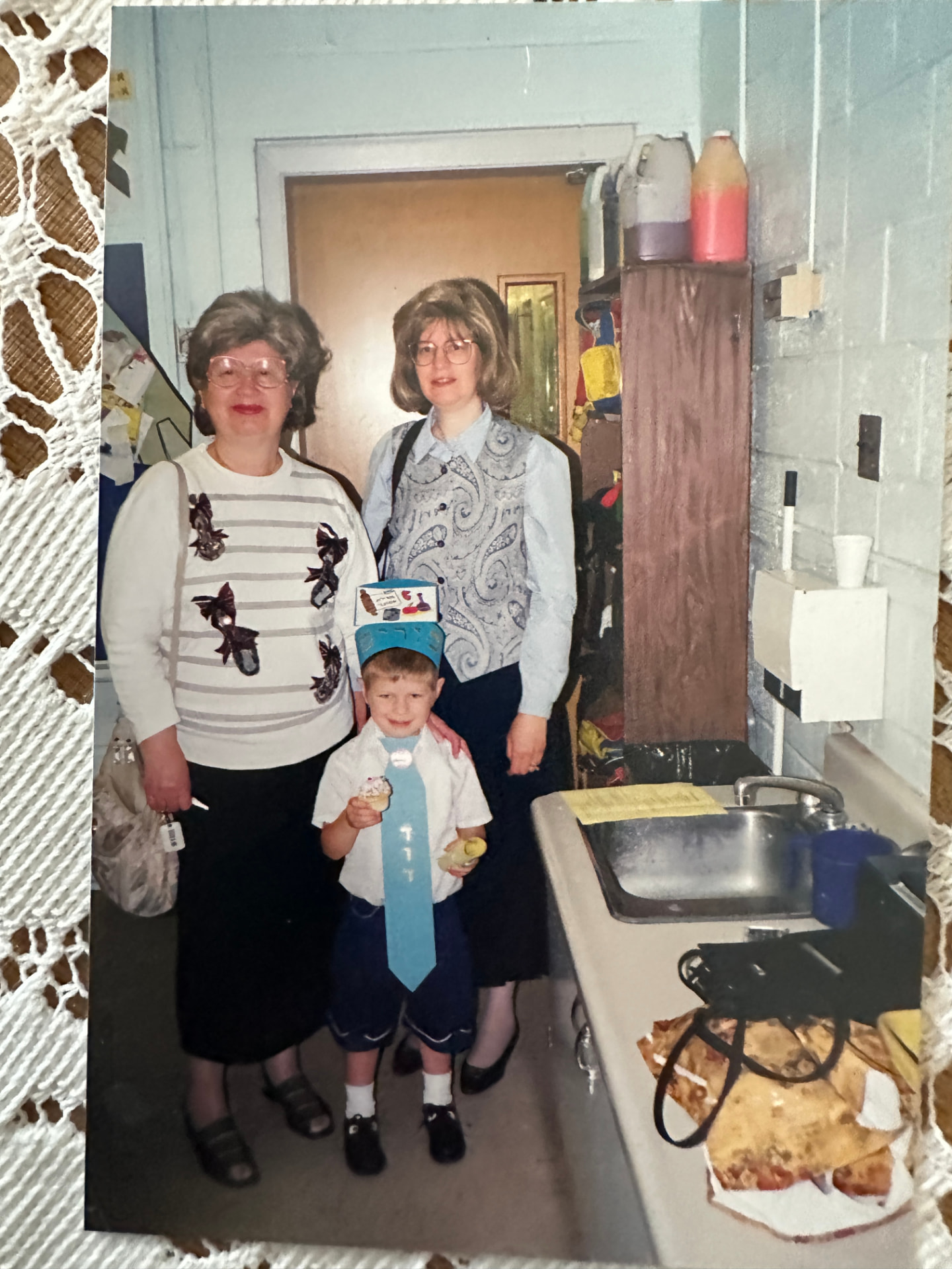 Bobby and her daughter at a school party with a grandson in his paper crown