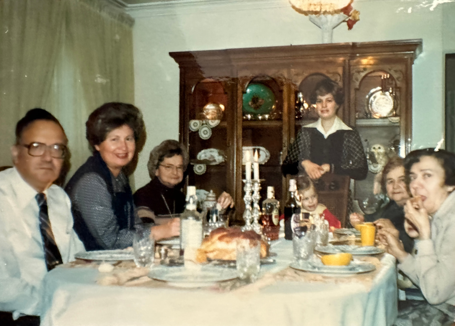 A Shabbos table at home, family gathered around the challah and candles