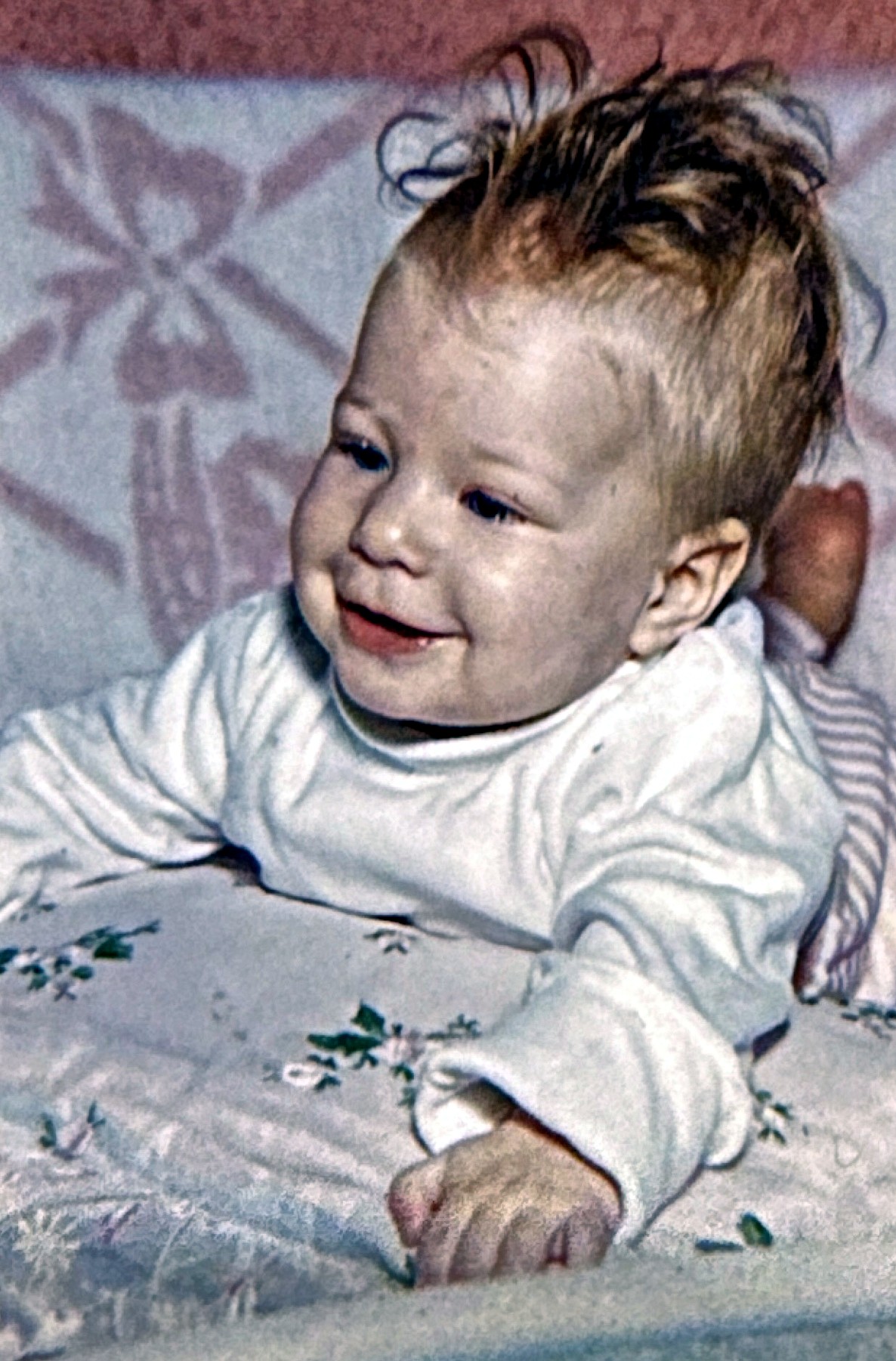 A Rubenstein baby propped up smiling on an embroidered blanket