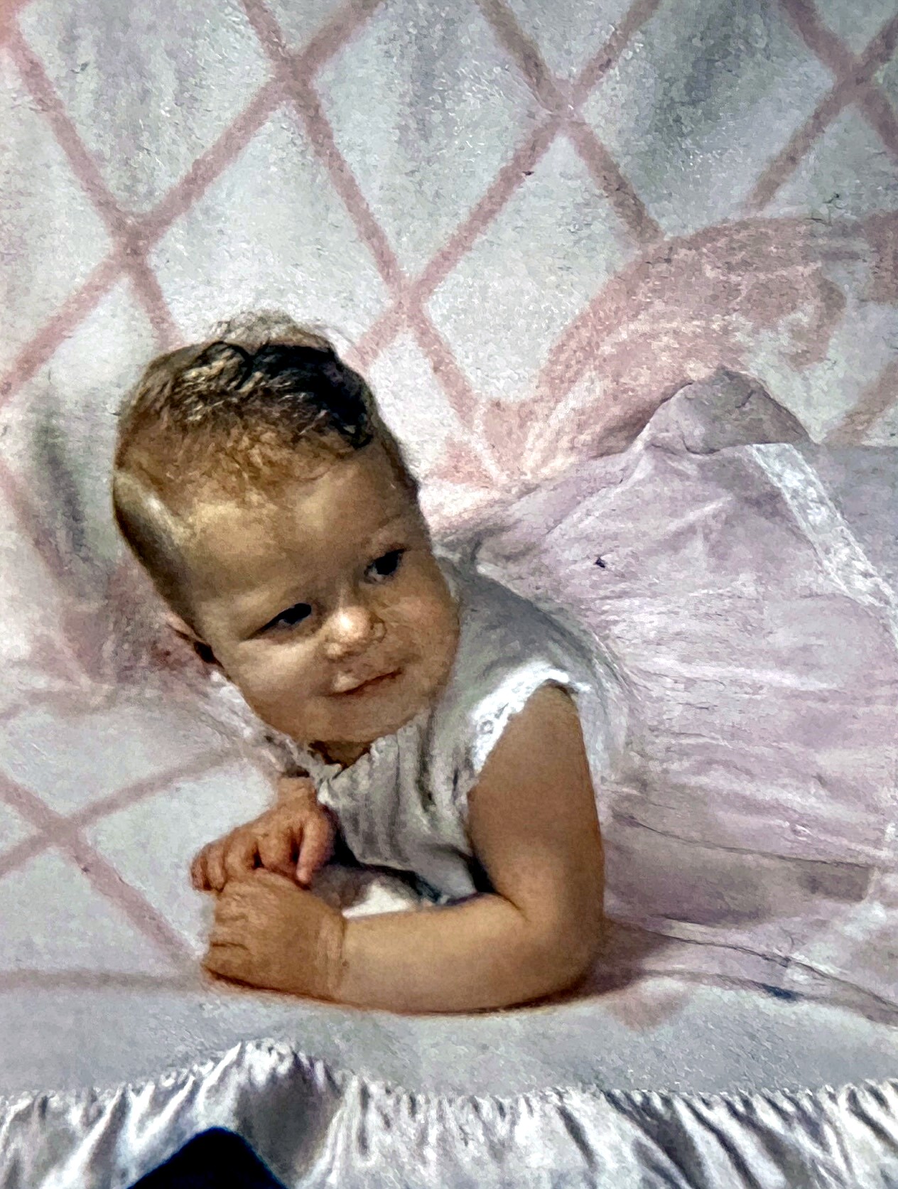 A Rubenstein baby on a pink quilt resting on her arms