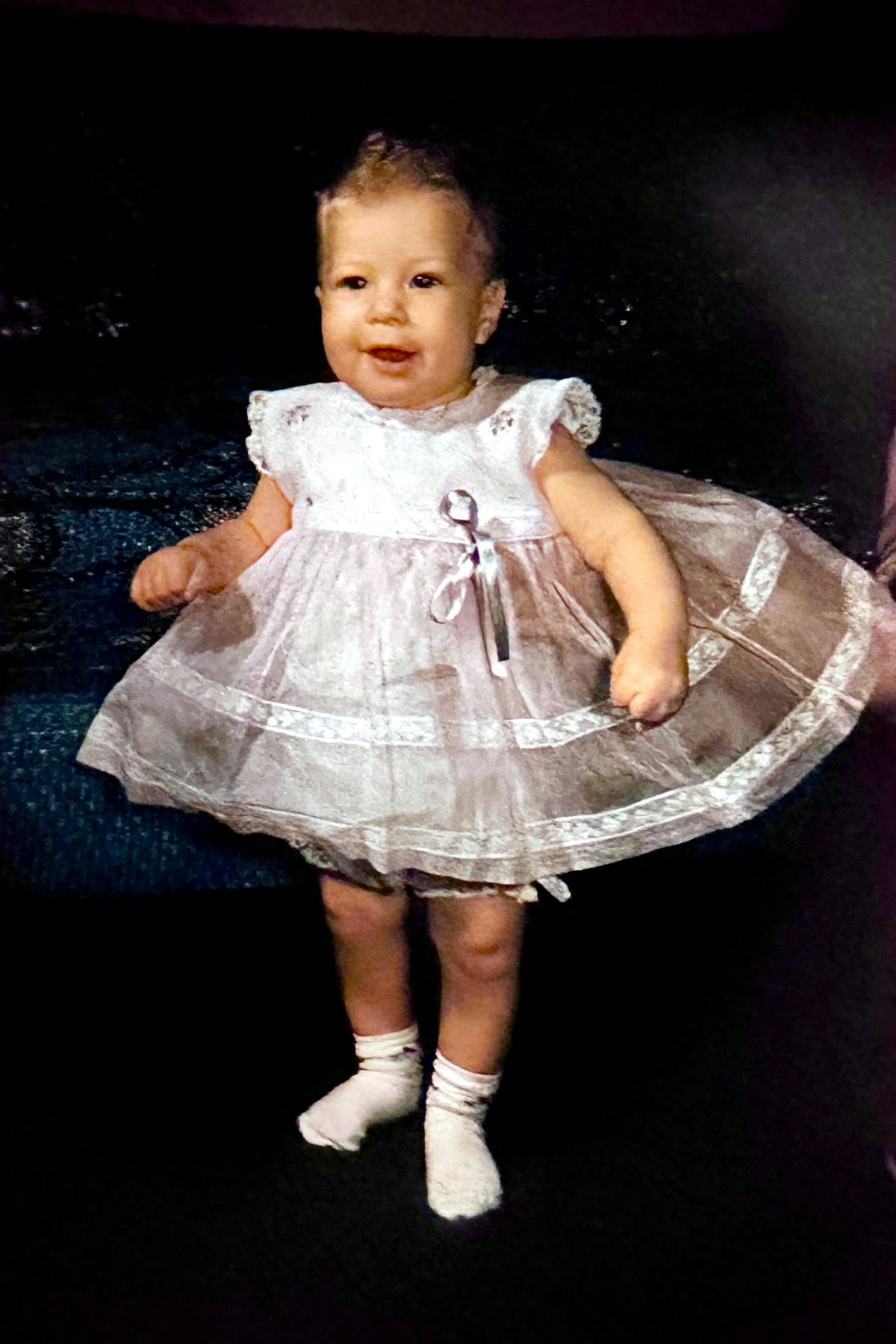 A Rubenstein baby girl standing in a lace party dress
