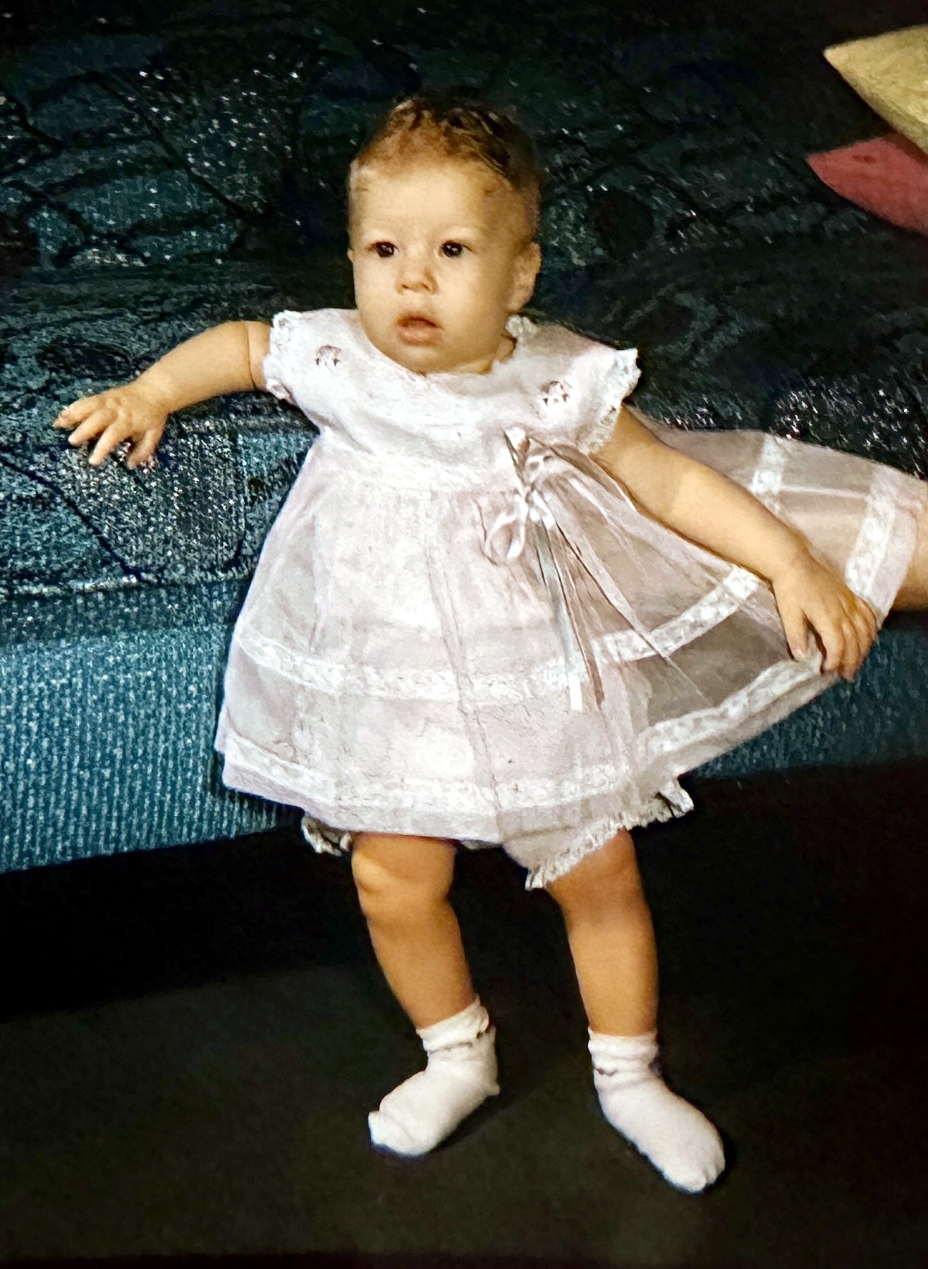 A Rubenstein baby girl in a white lace dress and socks